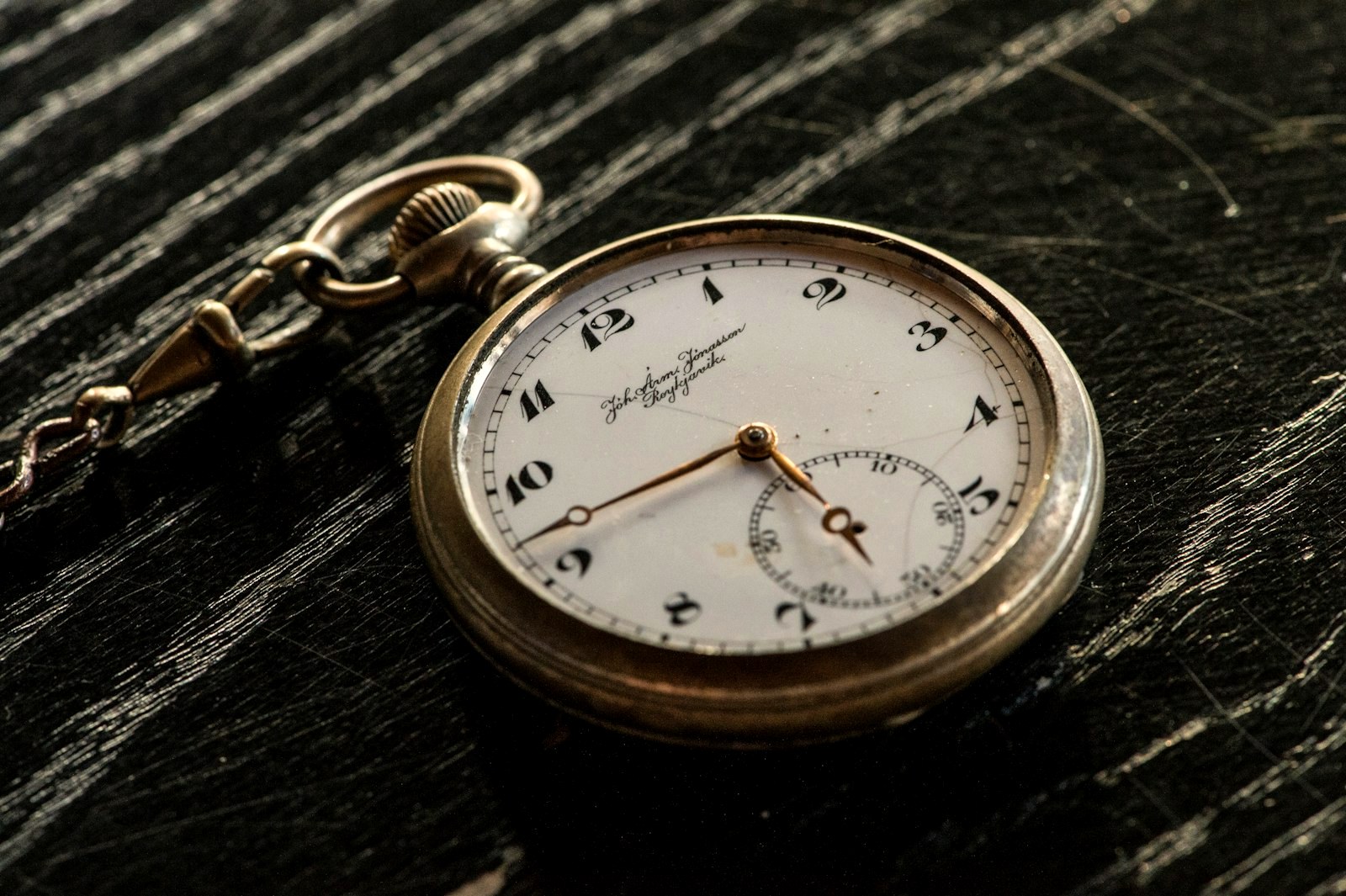 A pocket watch resting on dark scratched wood, a workbench heirloom