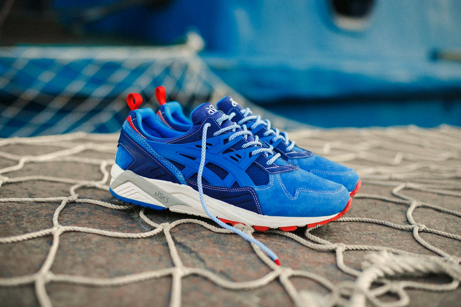 A pair of blue suede sneakers with red accents on a fishing net