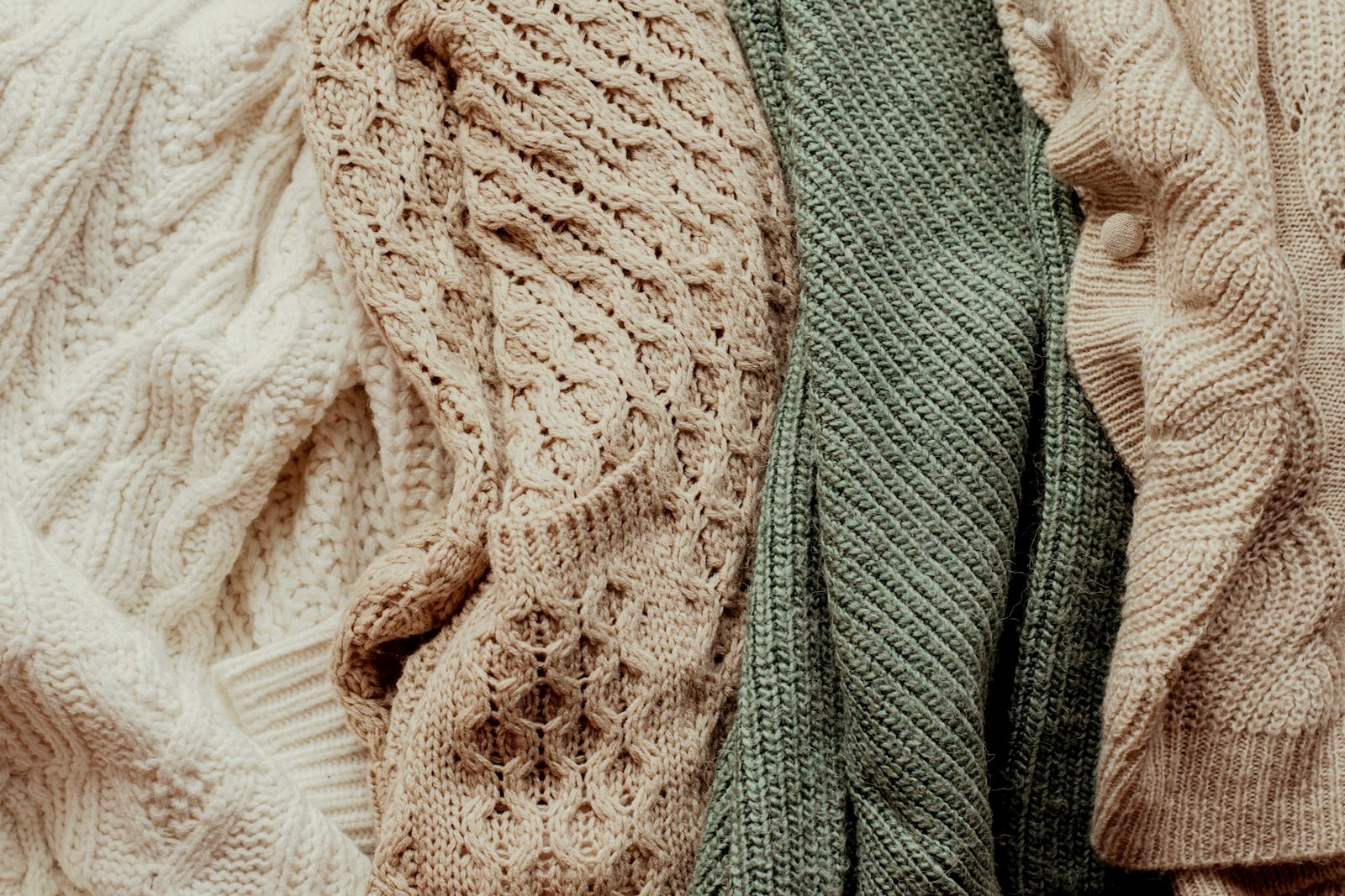 Close-up of knitted textures: cream cables and openwork stitches beside a sage rib