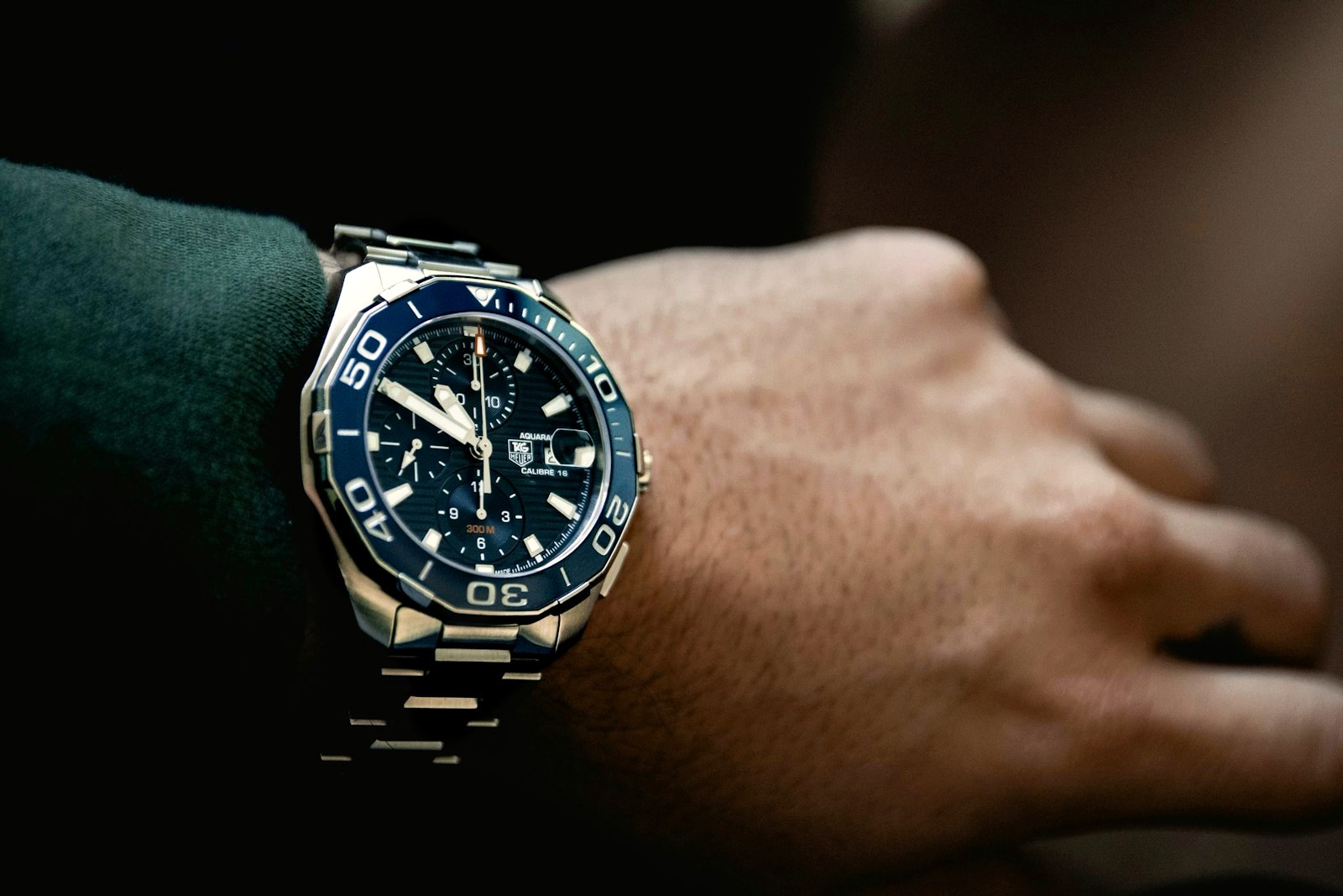 A steel dive chronograph on a bracelet seated on the flat of a wrist behind the wrist bone, a dark knit cuff above it