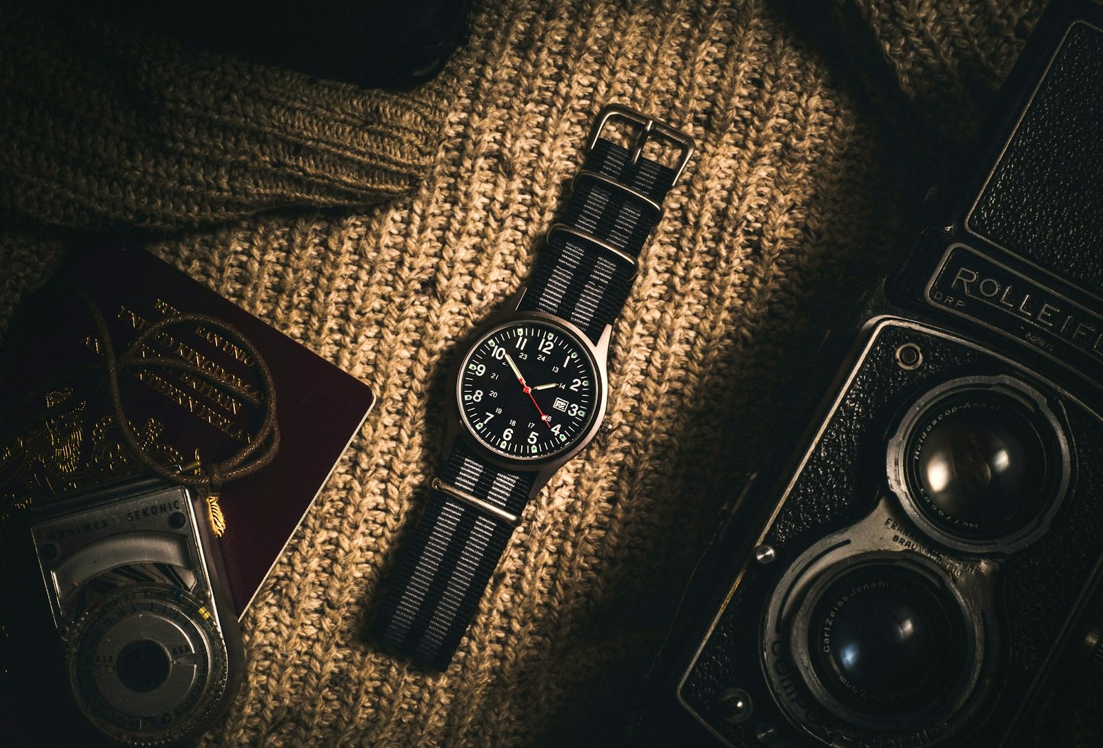 A travel flat lay of a field watch, cameras and a folded knit, packed for a trip