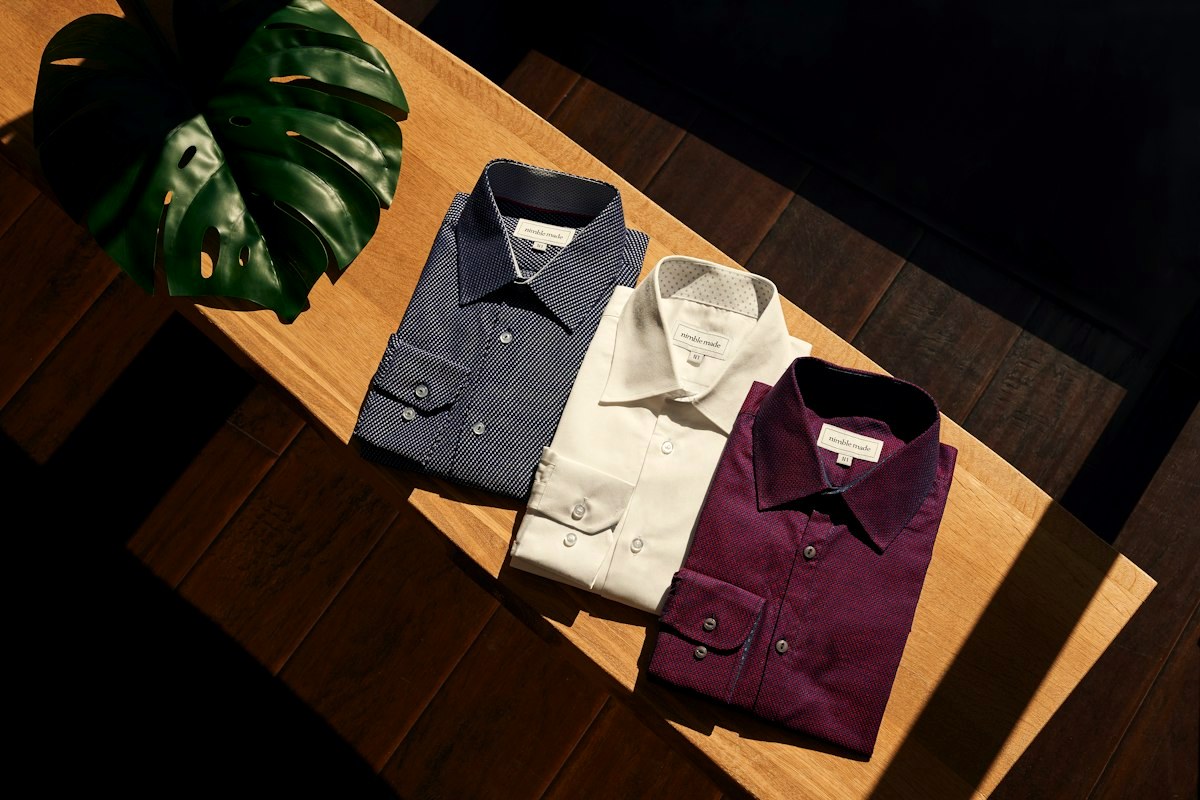 Folded men's shirts in navy, white and burgundy laid out on a wooden table