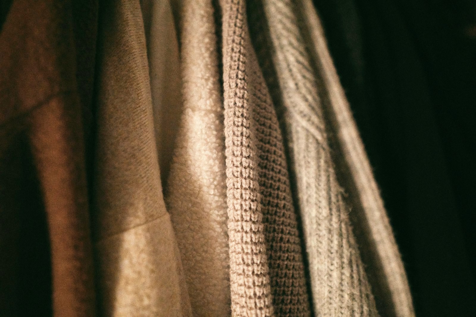 Knitwear hanging in close view, camel and cream gauges catching warm light