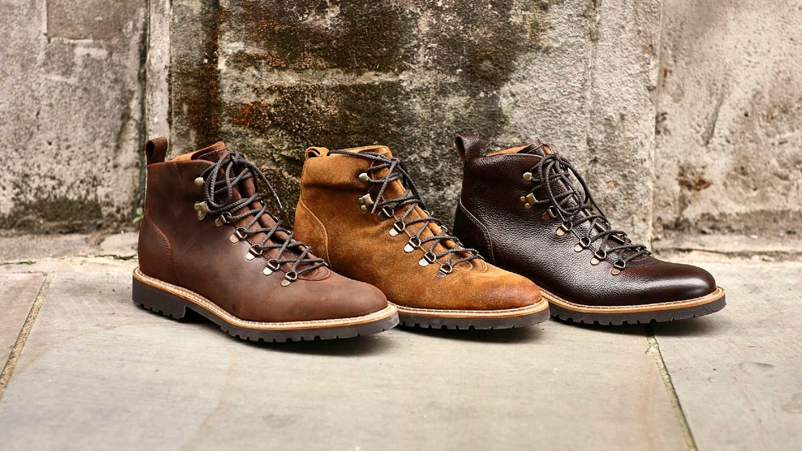 Three leather hiking boots in brown tones lined up against a stone wall