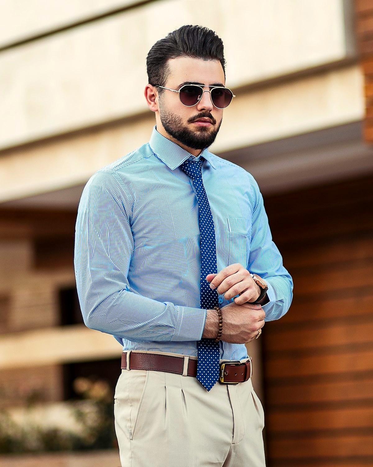 Man in a blue striped shirt and polka-dot tie adjusting his cuff