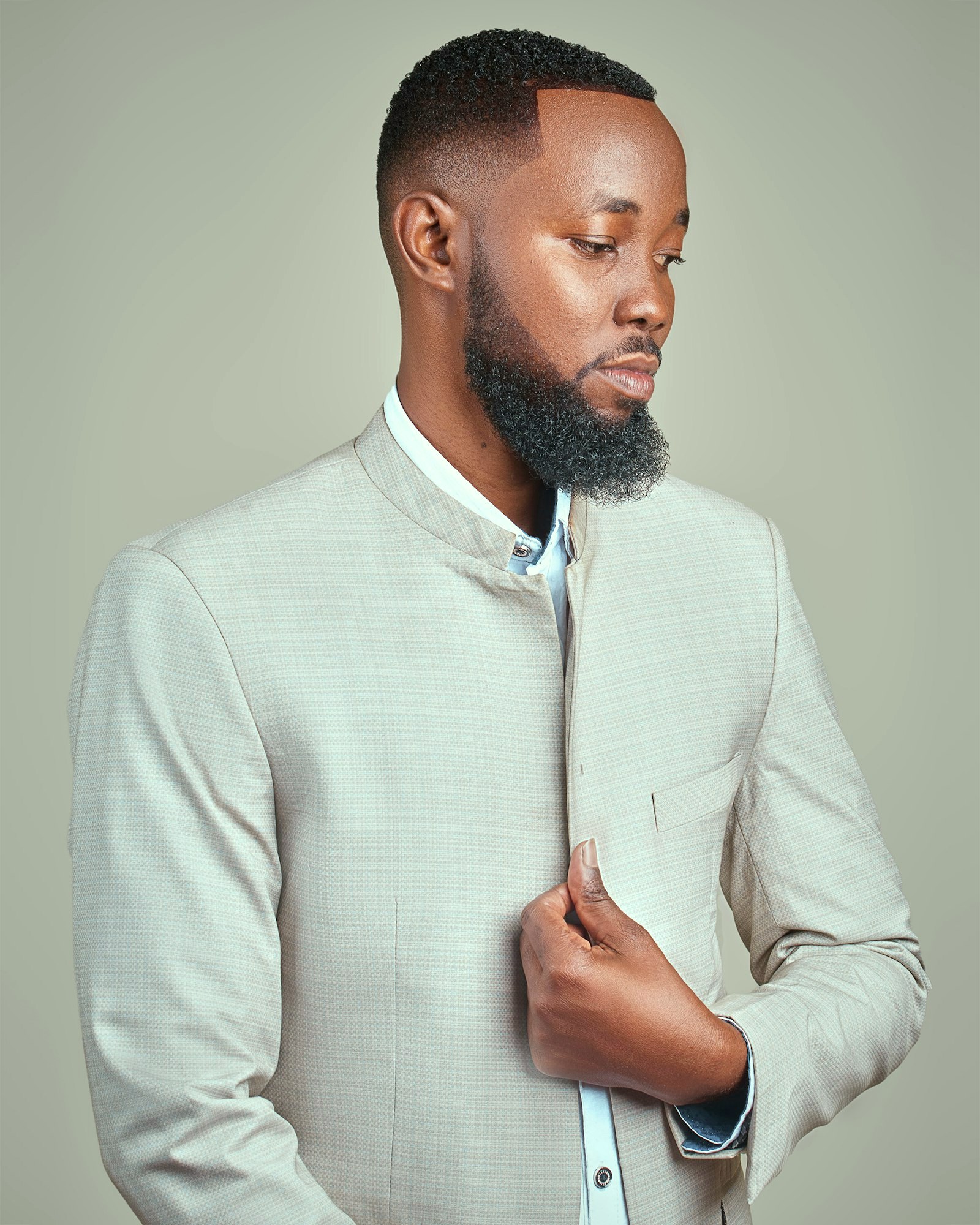A man in a pale unstructured jacket with a stand collar, in profile, hand at the placket