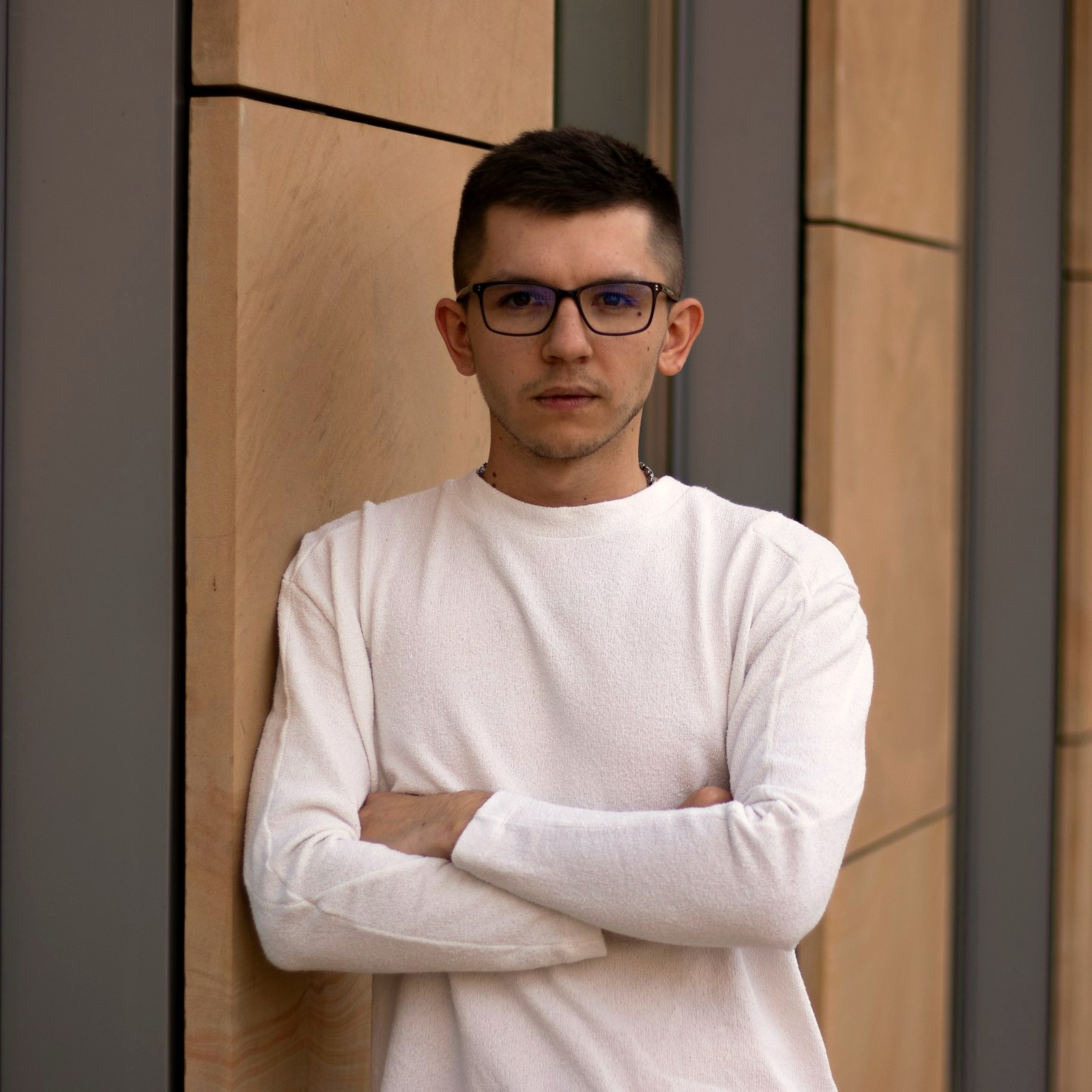 Young man in a white crewneck sweater wearing black frames with deep lenses