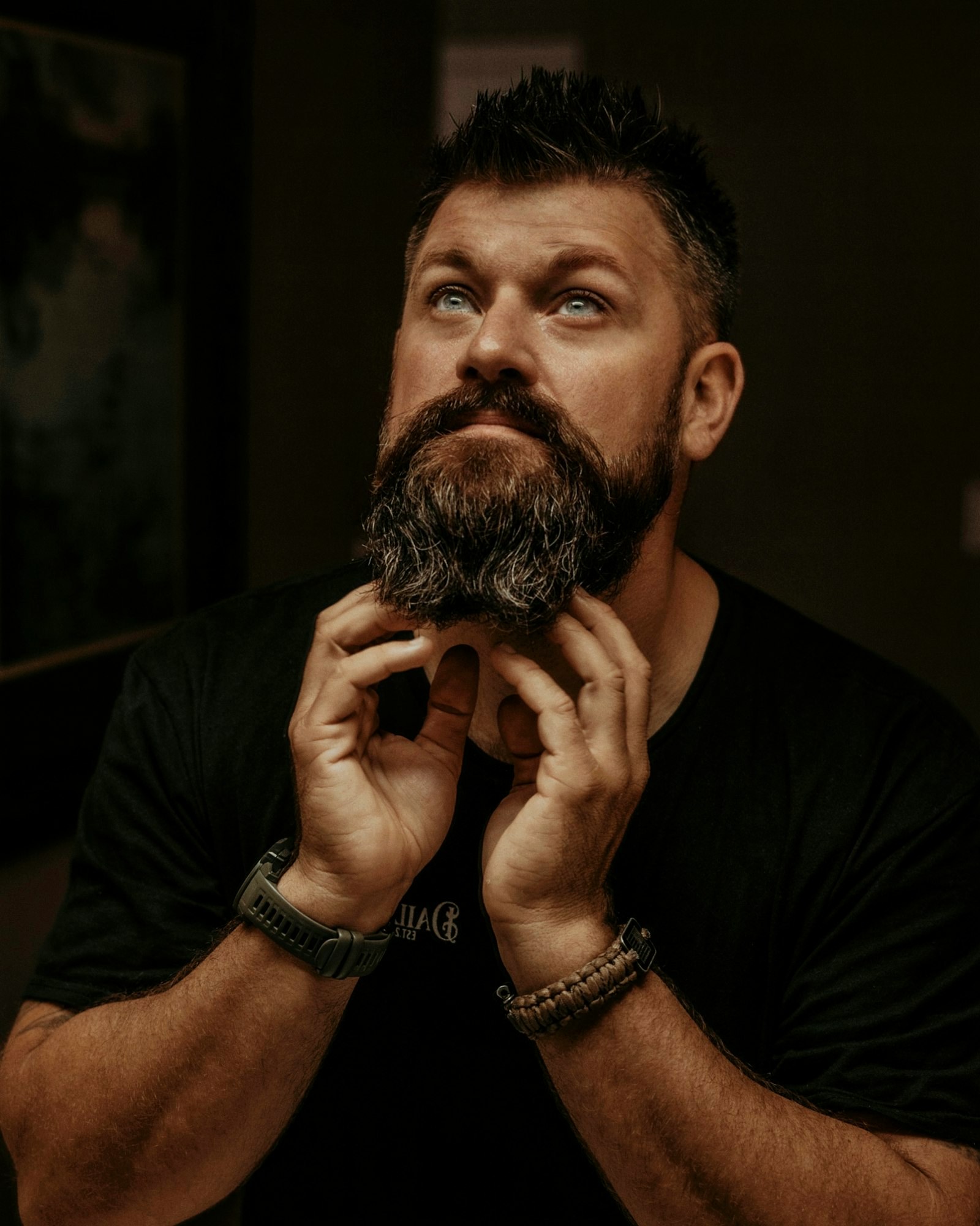 Man with a full beard and strong natural brows in low light