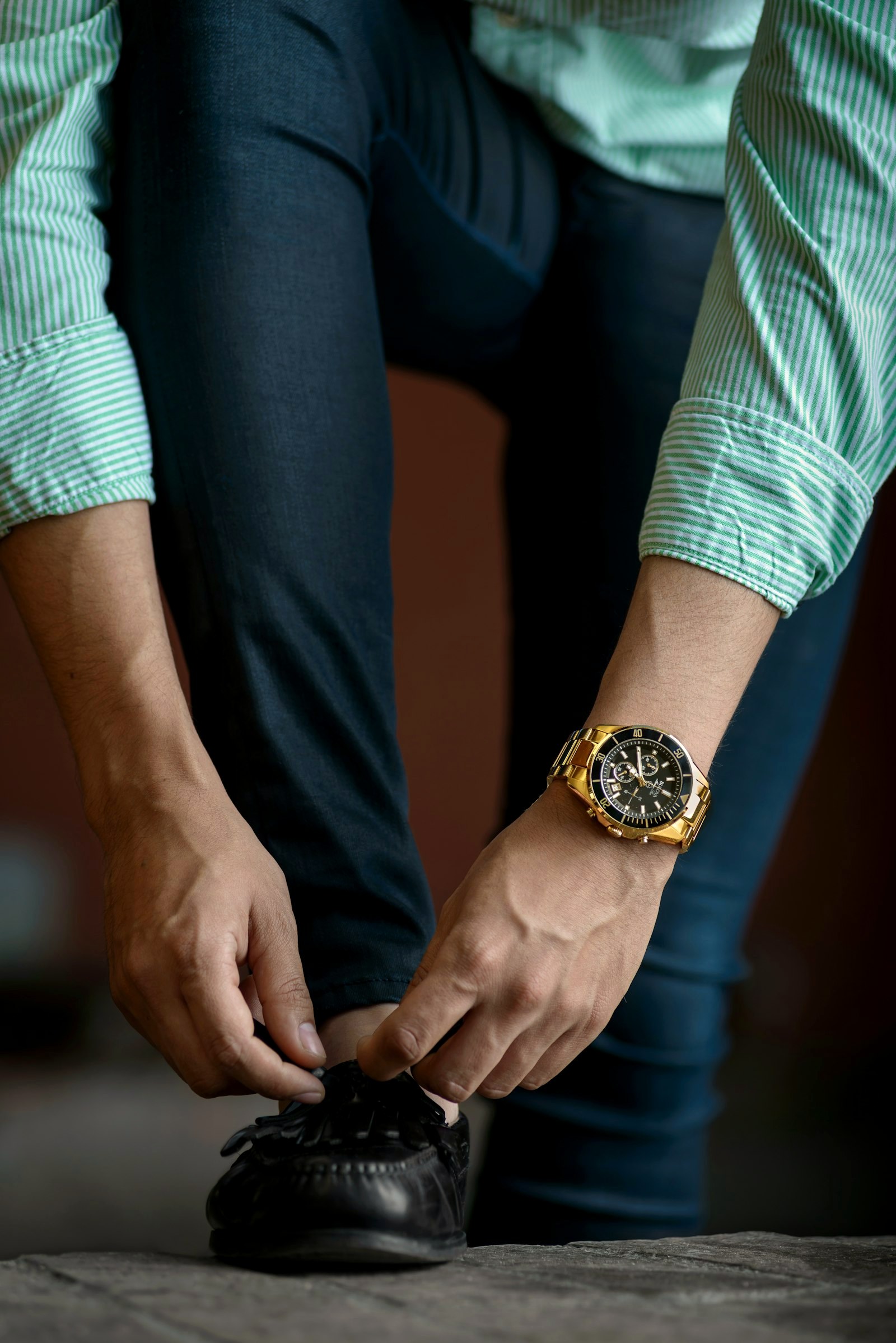 A tailored trouser hem breaking over a loafer as the wearer ties his shoe