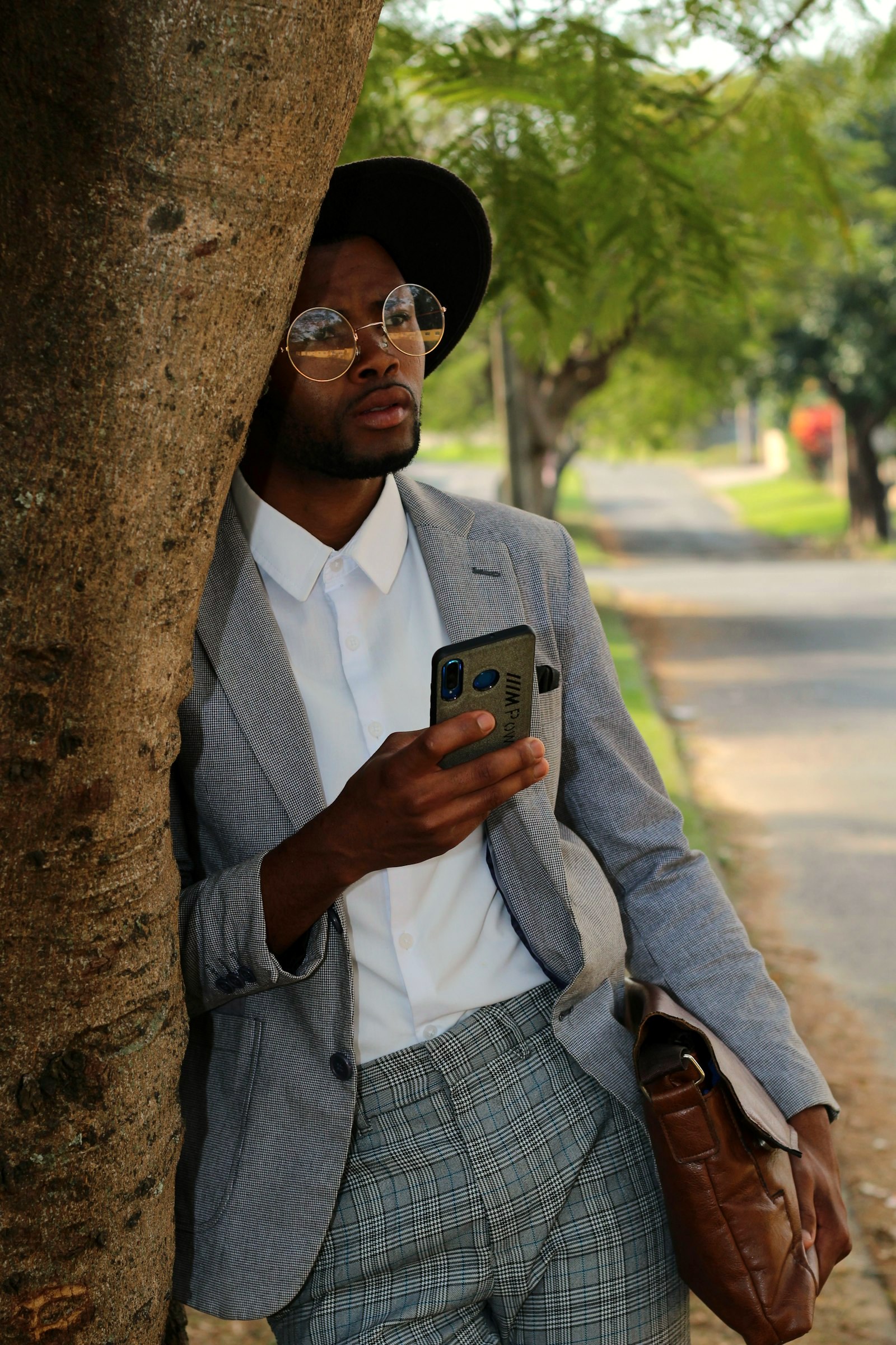A grey check suit and white shirt worn on a leafy street, the jacket's breast pocket standing empty at reading distance: the inch this brief rules, unfilled in the frame
