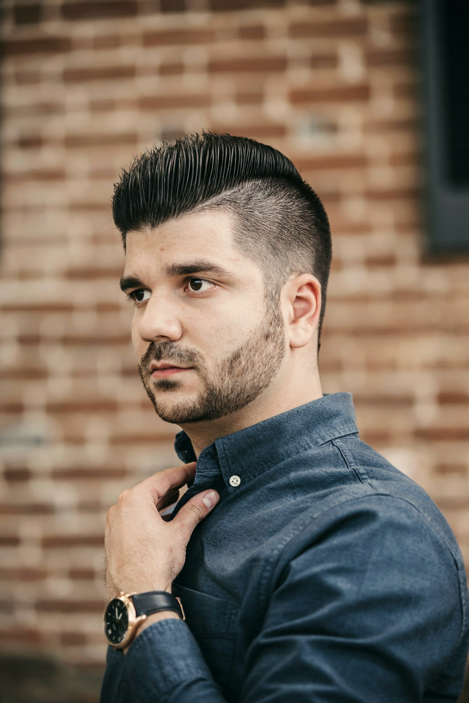 Man with a full, natural brow and short faded haircut against a brick wall