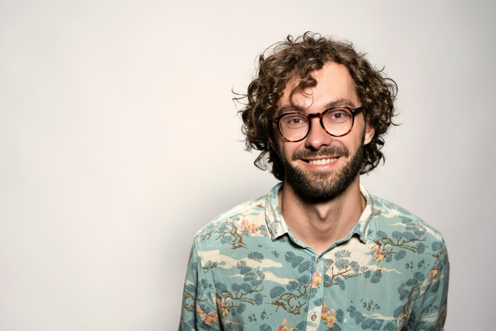 Young man with curly hair and a short beard wearing round tortoiseshell frames at an honest width