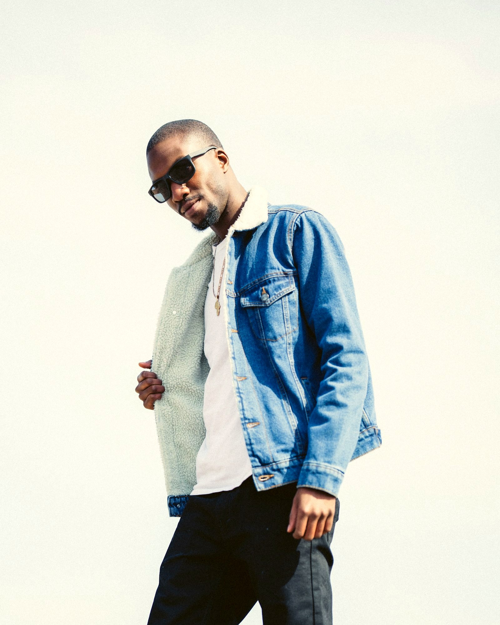 A man in a sherpa-collared denim jacket over a white t-shirt in bright daylight