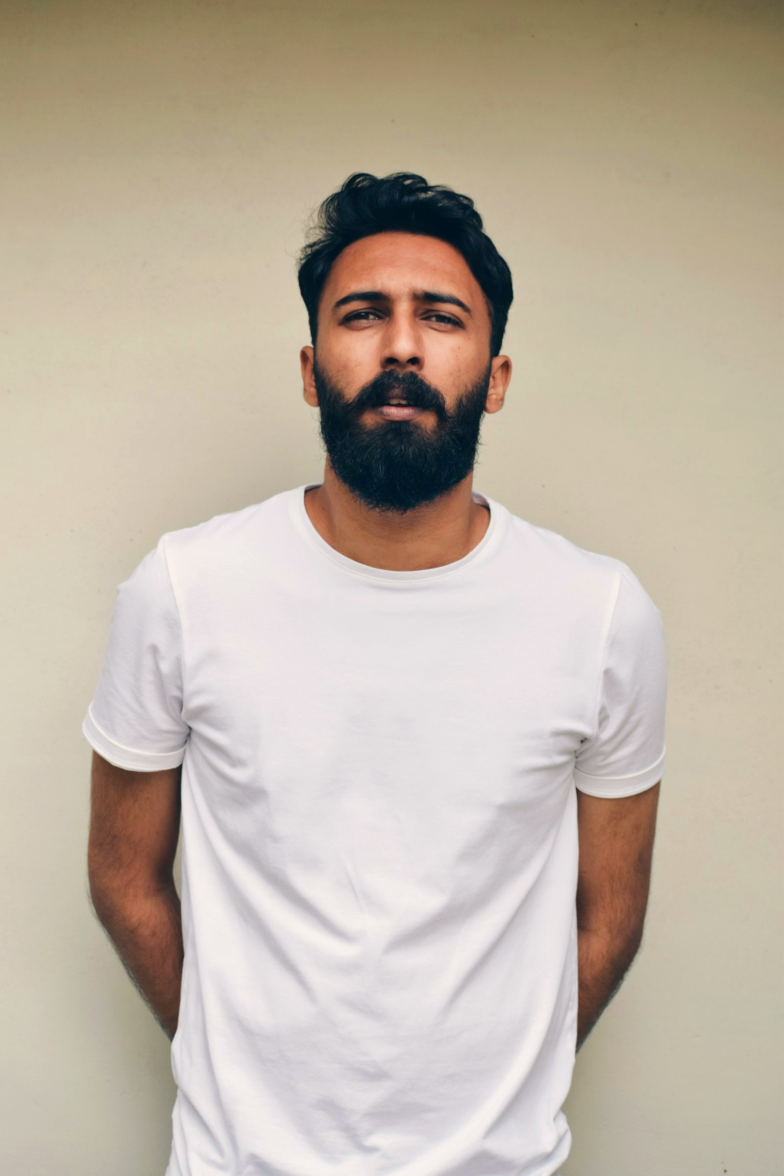 Young man with textured hair worn up and a full beard kept neat, in a plain white t-shirt