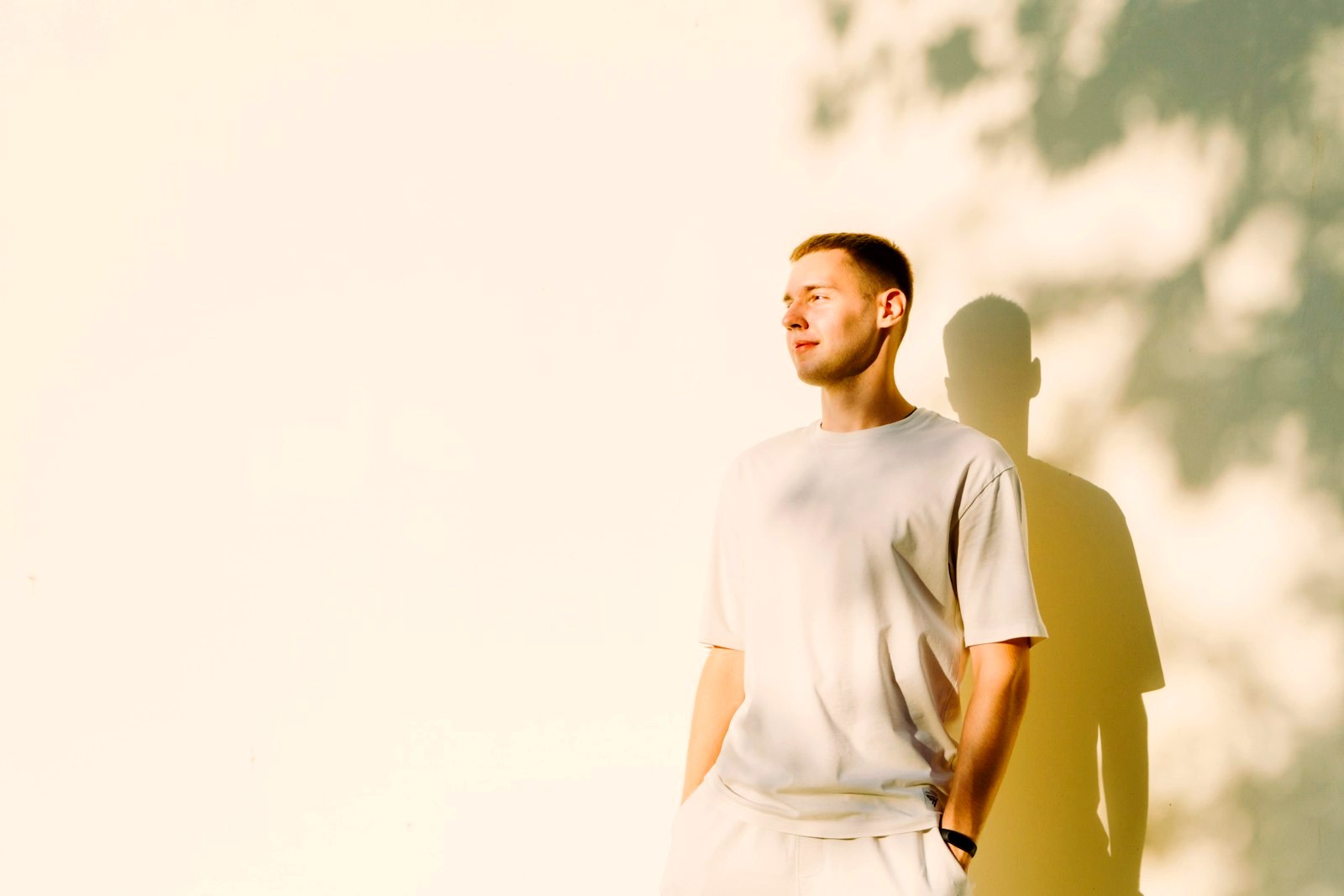 Man in a white t-shirt standing in hard sunlight against a wall