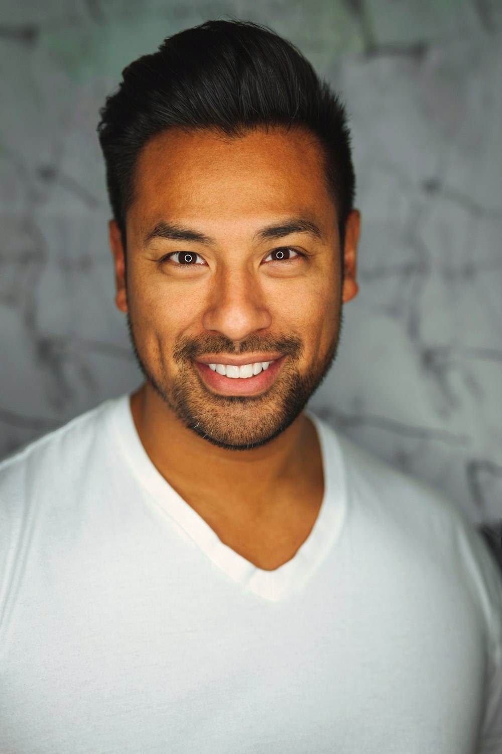 Young man with a softer, fuller face and hair swept up with height, in a white v-neck t-shirt