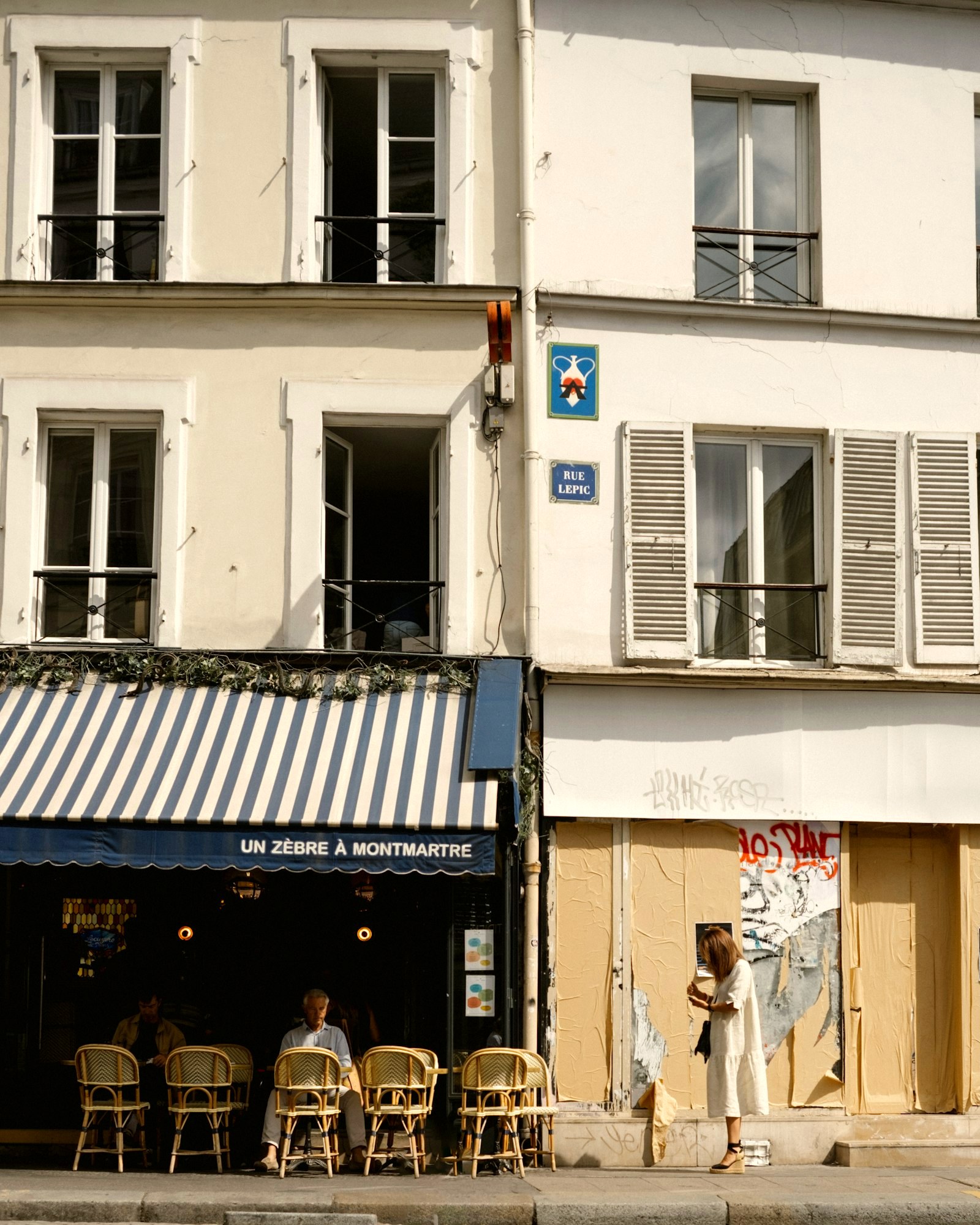 A small Paris cafe with a blue-striped awning under shuttered facades, Montmartre