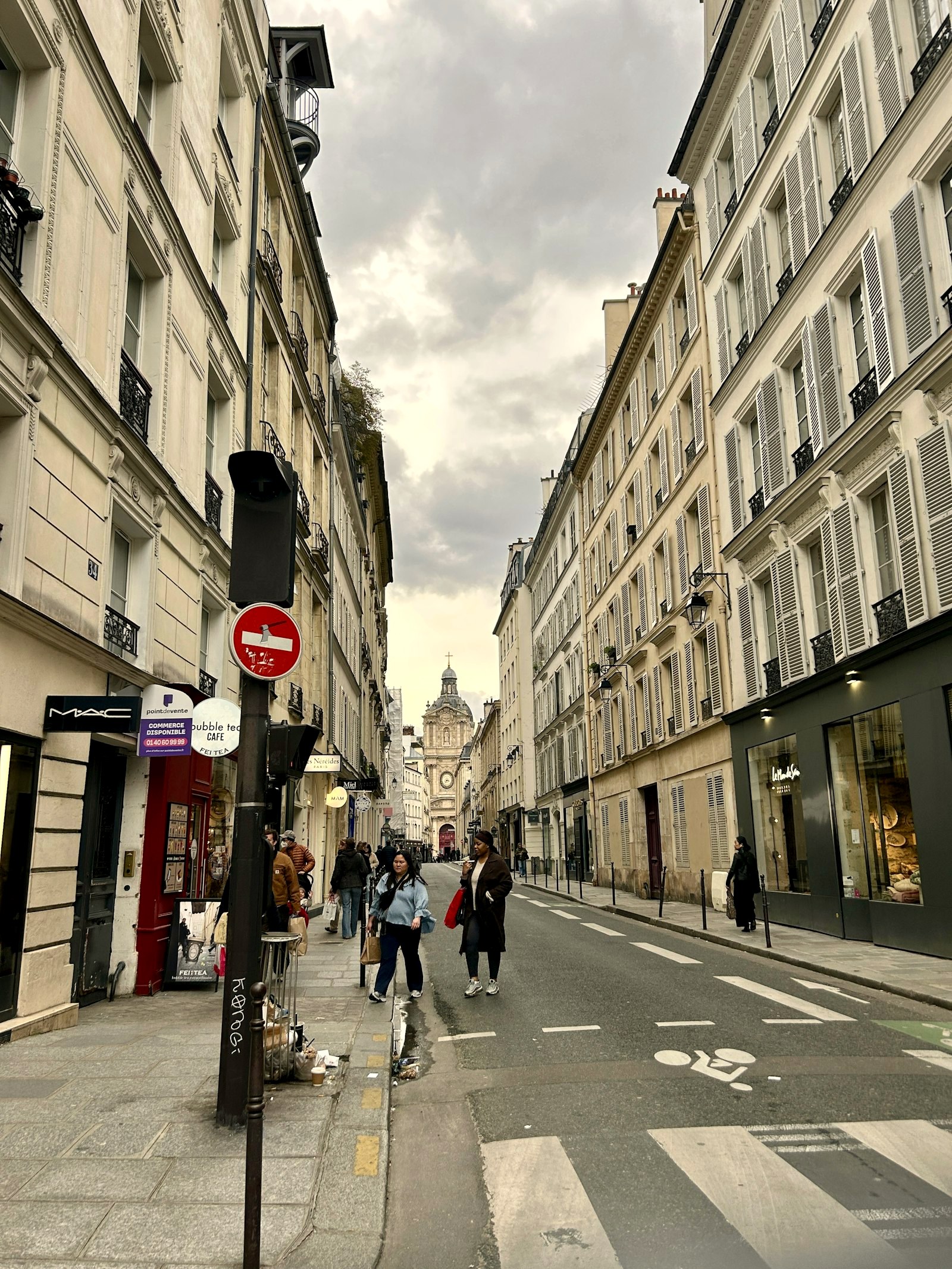 A Paris shopping street with pedestrians in coats, a domed church at the end of the road
