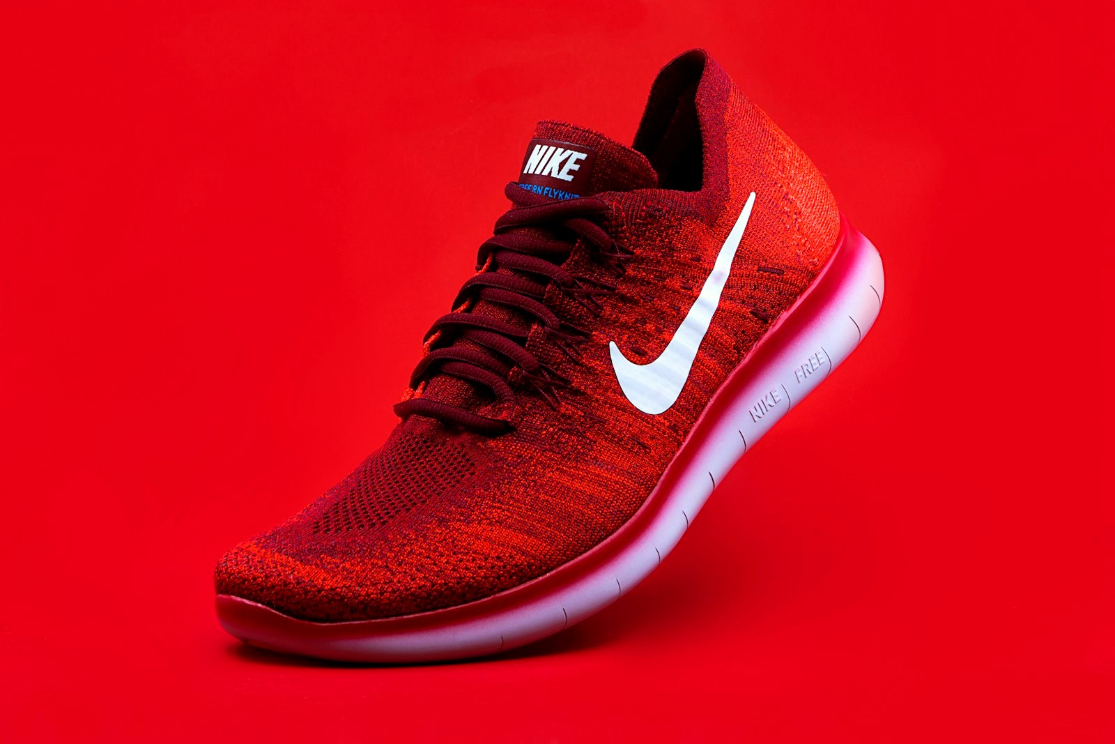 A red knit Nike running shoe photographed against a red studio background