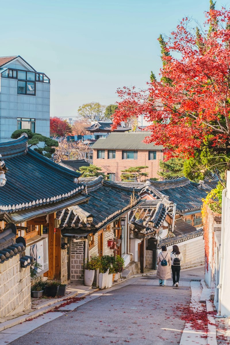 A lane of tiled hanok roofs in Bukchon, Seoul, long coats walking away