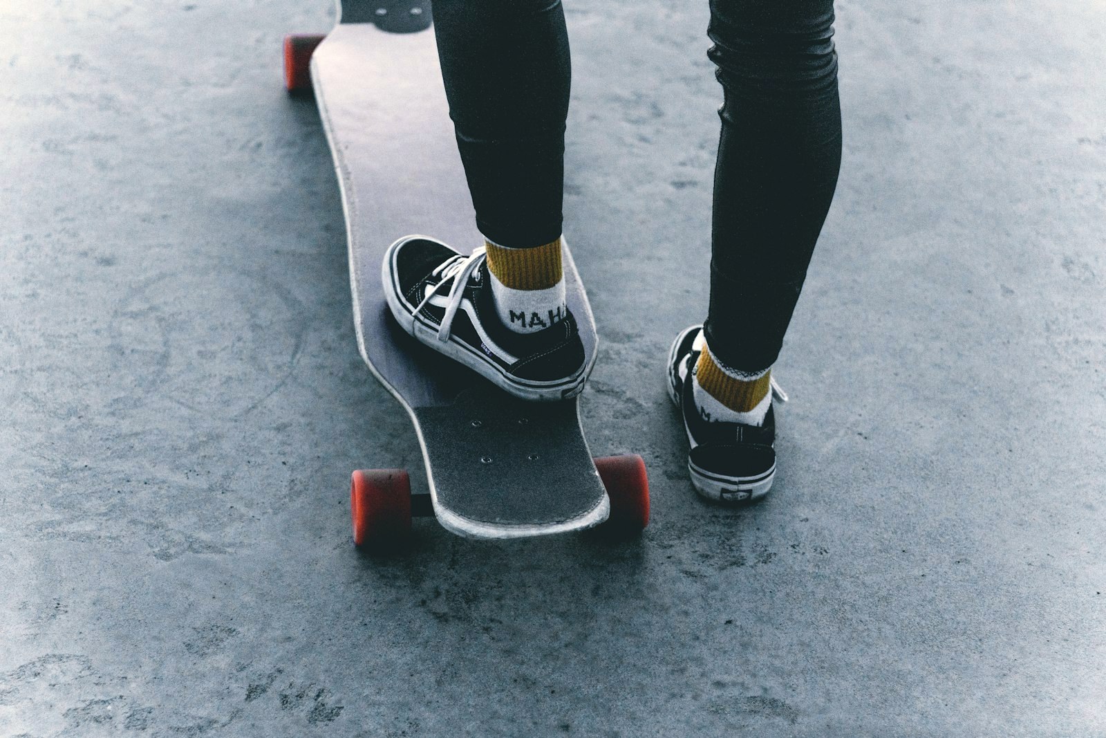 Worn black skate shoes on a rider's feet, one foot on a longboard