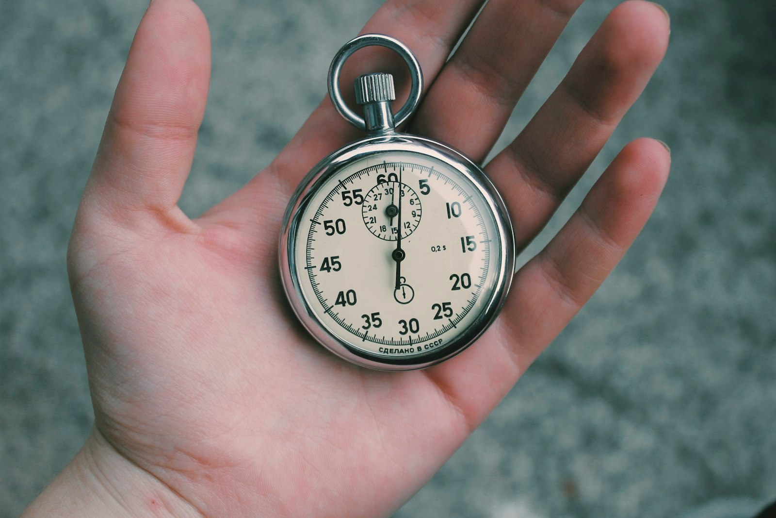 A vintage metal stopwatch held in the hand outdoors, an instrument, not an heirloom