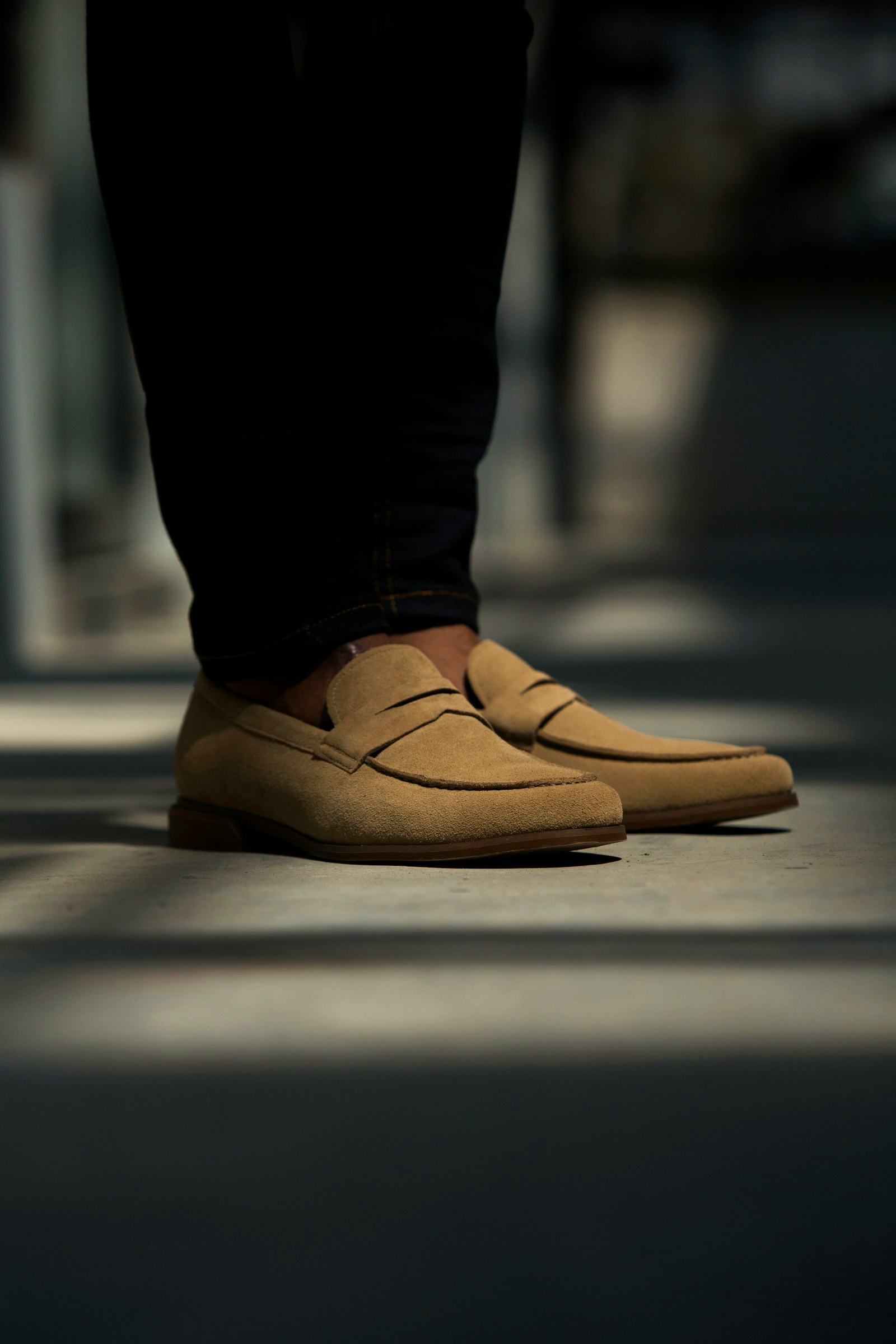 Tan suede penny loafers on feet on a city pavement, long shadows
