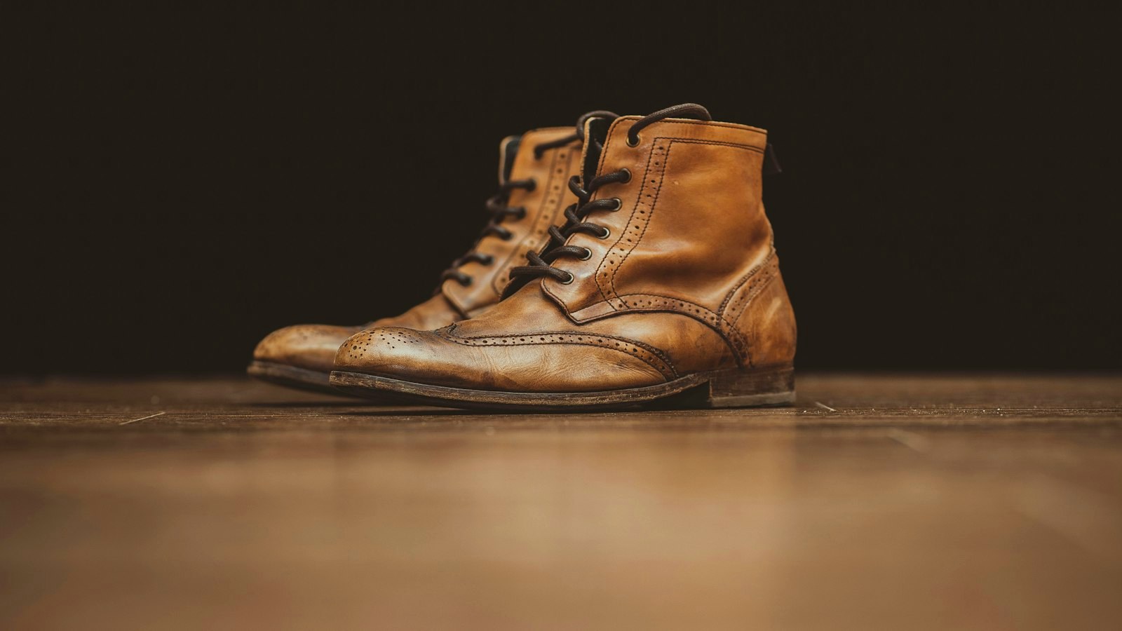 A worn pair of tan leather brogue boots on a wooden floor