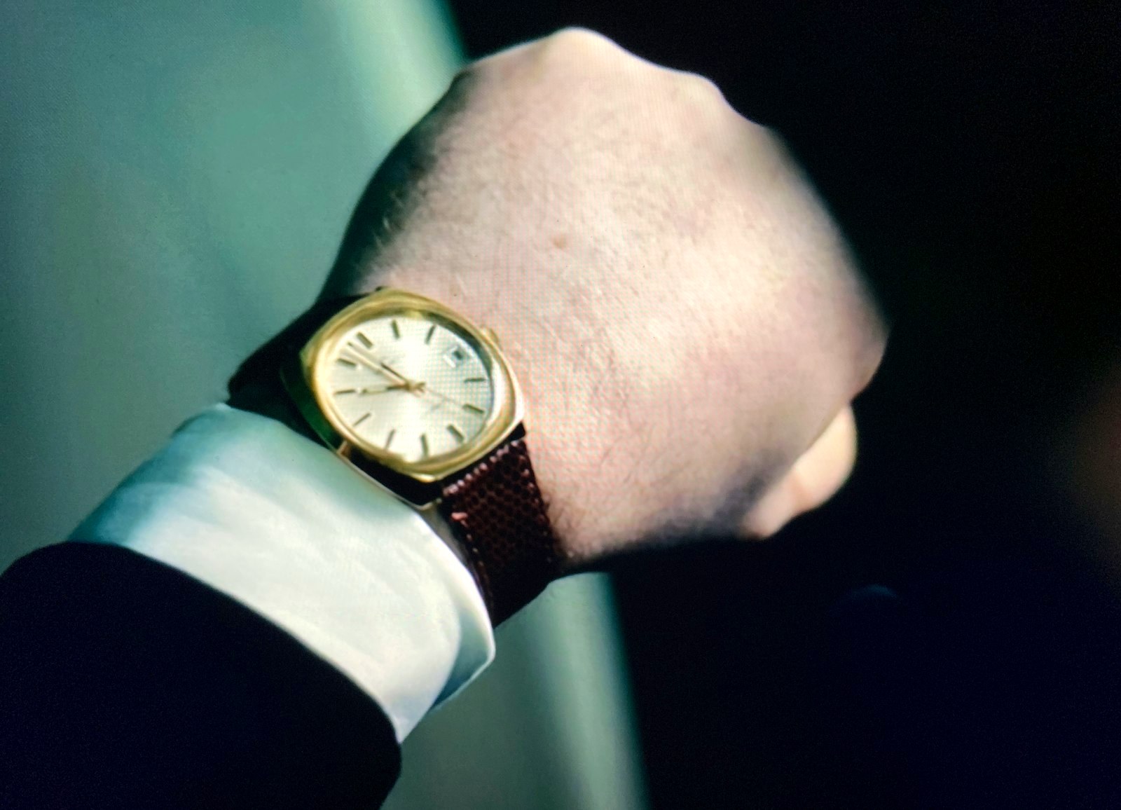 Gold-tone dress watch on a brown leather strap at a shirt cuff