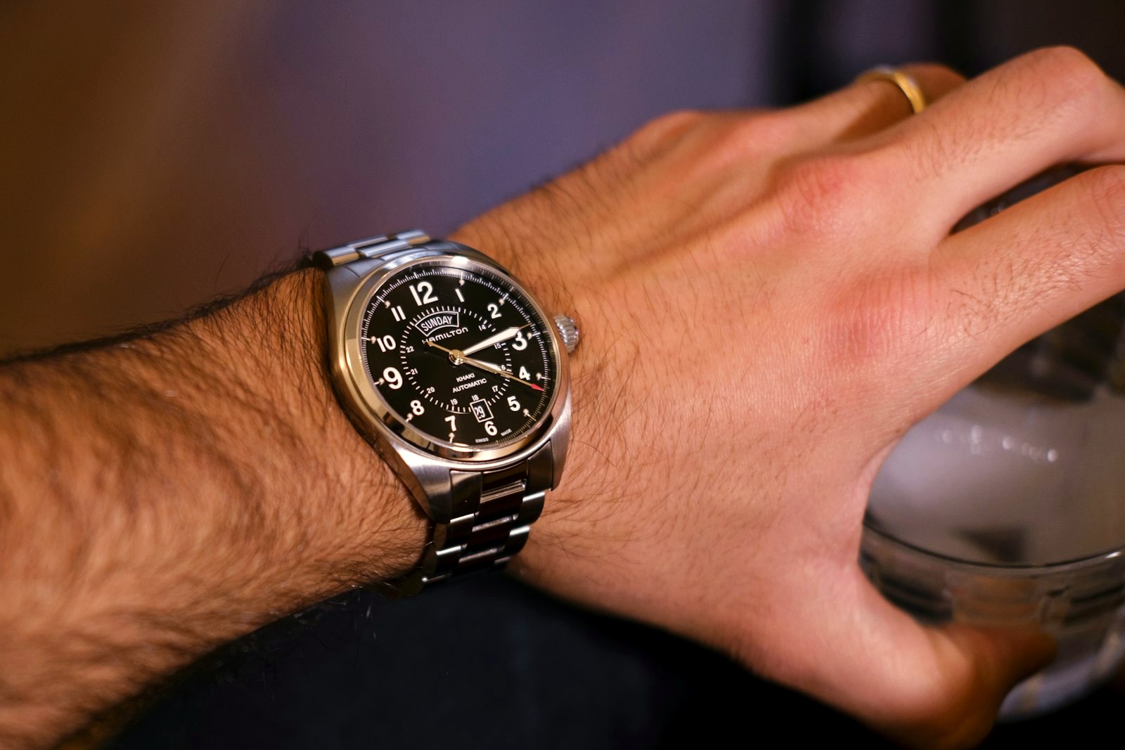 Field watch with a black Arabic-numeral dial on a steel bracelet, worn on a wrist