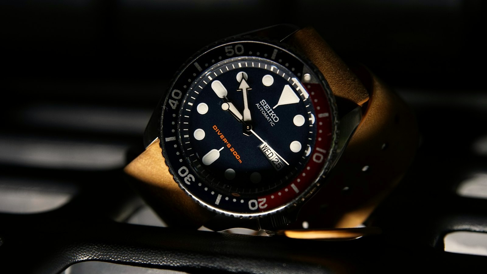 Seiko diver-style watch with a two-tone bezel on a tan strap in low light