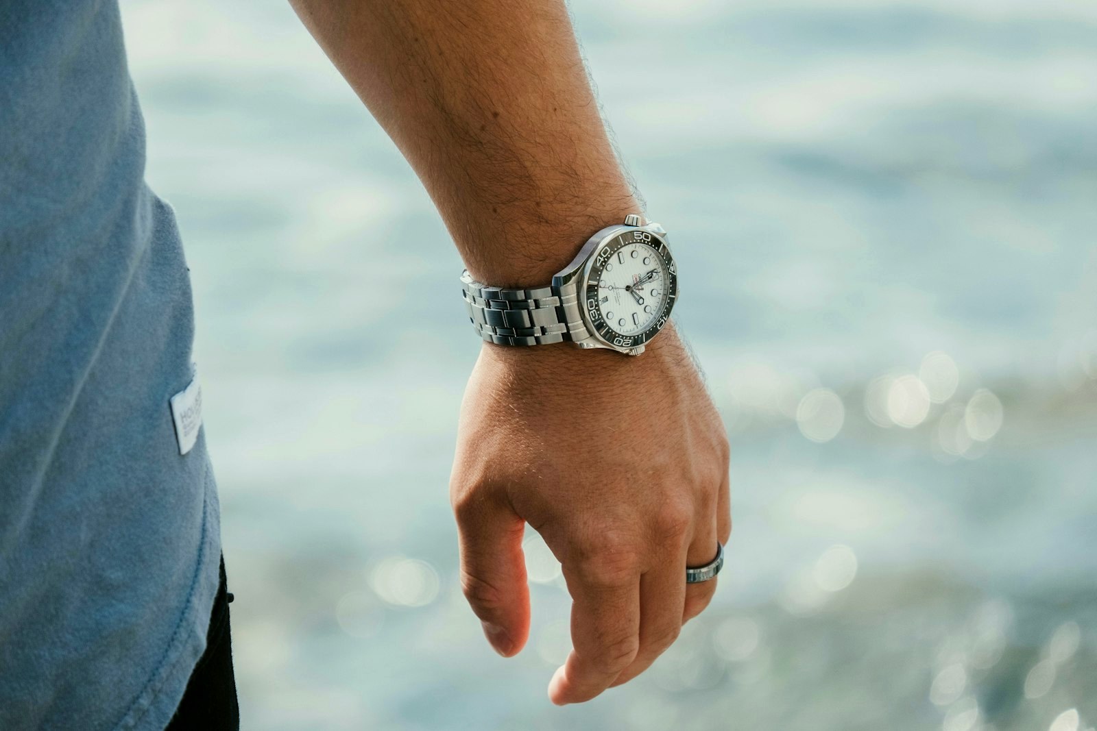 Man's wrist wearing a light-dial steel bracelet watch beside the sea in soft light