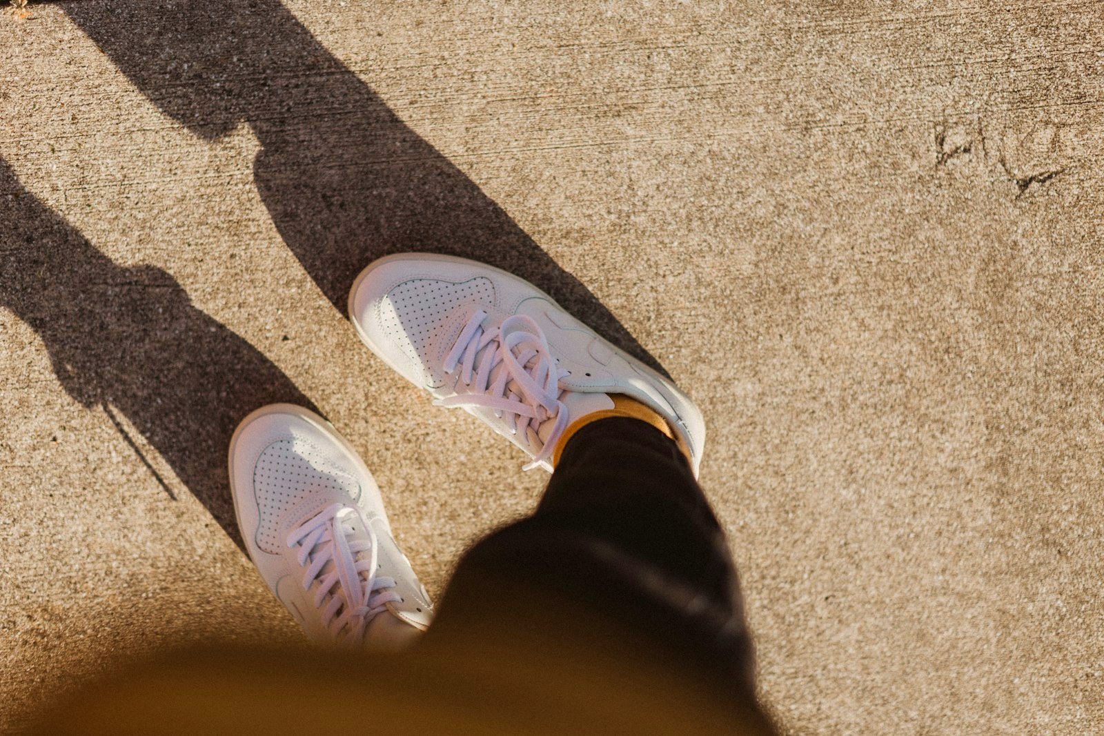 White sneakers on feet, seen from above on sunlit concrete, long shadows
