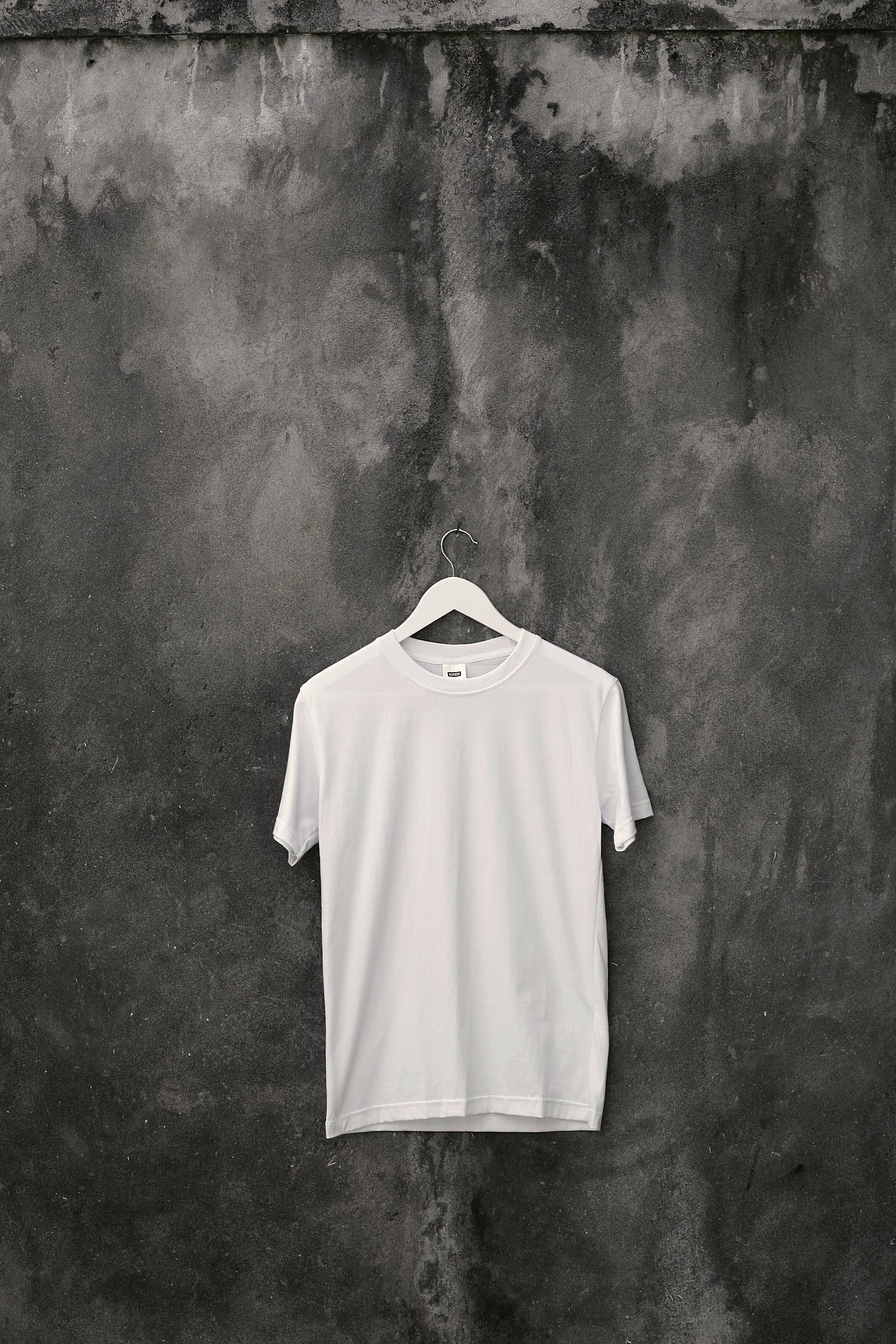 Plain white t-shirt on a hanger against a weathered concrete wall