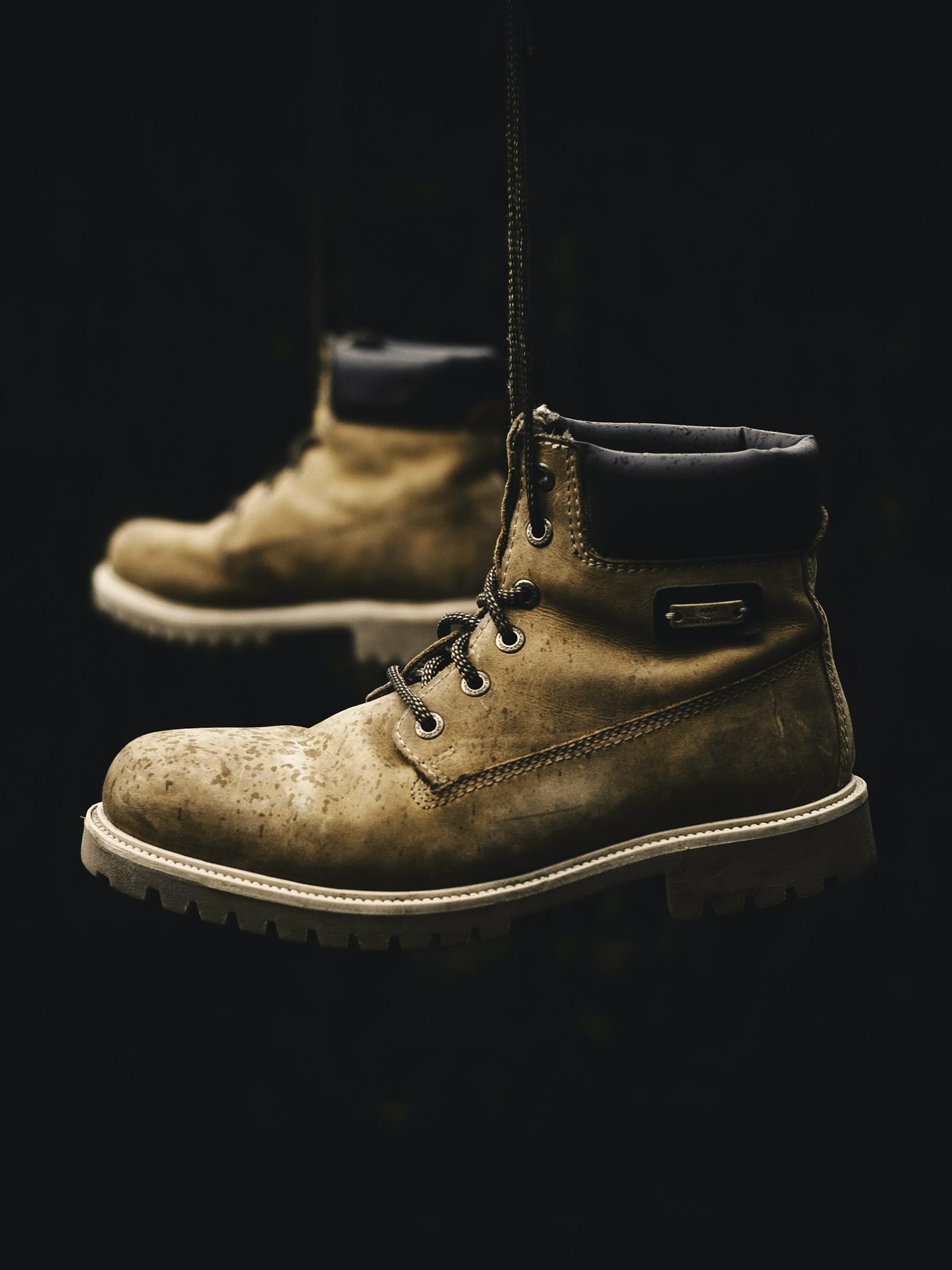 Worn work boots hanging by their laces against a dark backdrop