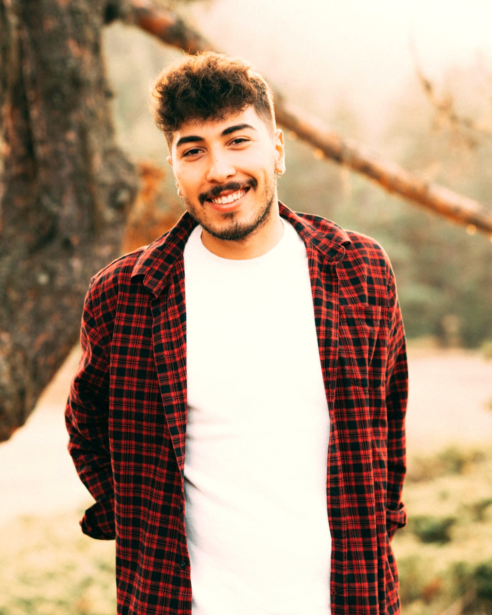 Young man with a curly fringe worn forward, in a flannel overshirt over a white t-shirt