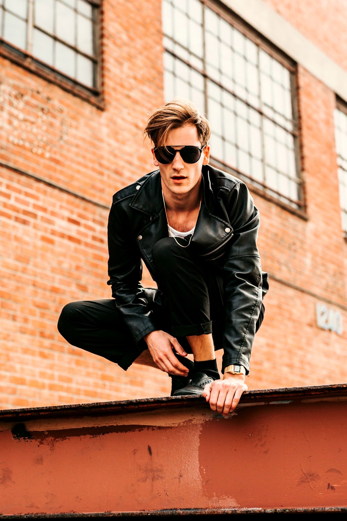 Young man in a black leather jacket over a white t-shirt against a brick warehouse wall